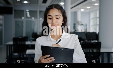 La secrétaire de jeune femme écrit les détails de la tâche écrivant les données dans le presse-papiers rend les rendez-vous quotidiens une petite fille adorable stagiaire écoute le superviseur prend Banque D'Images