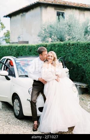 Milan, Italie - 07.04.21: La mariée et le marié sont assis sur le capot d'une Fiat 500 blanche dans un jardin verdoyant Banque D'Images