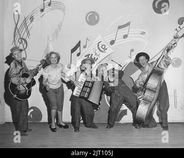 La musique dans le 1950s. Un groupe de cinq membres sur scène tous habillés et jouant heureusement. Deux des hommes portent un costume Zoot typique, un costume pour hommes avec un pantalon à taille haute et à larges jambes, et un long manteau avec des revers larges et des épaules rembourrées larges. Le procès de zoot a été controversé en 1940s. Le mot Zoot vient probablement d'une duplication de suit. Suède 1940s Conard Réf. 240/2 Banque D'Images