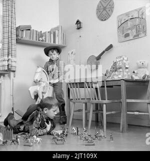 Garçons dans les 1950s. Deux garçons dans leur salle de jeux sont habillés comme des cow-boys. L'un est à cheval en bois et l'autre à jouer avec des personnages de cow-boys et d'indiens sur le sol. Suède 1953 Conard réf. 2273 Banque D'Images