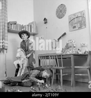 Garçons dans les 1950s. Deux garçons dans leur salle de jeux sont habillés comme des cow-boys. L'un est à cheval en bois et l'autre à jouer avec des personnages de cow-boys et d'indiens sur le sol. Suède 1953 Conard réf. 2273 Banque D'Images