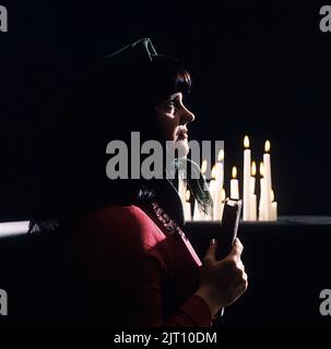 Église en 1970s. Une femme photographiée comme dans une église avec des bougies allumées en arrière-plan. Elle tient un livre de psaume usé ou la bible entre ses mains. Suède Banque D'Images