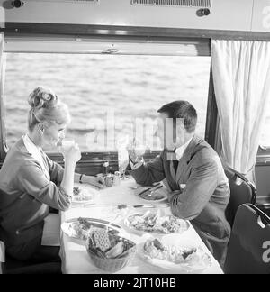 Voyage en train en 1960s. Un couple dans la voiture du restaurant du train est en train de savourer le dîner ensemble. Elle a une coiffure typique de 1960s. Suède 1960s Kristoffersson réf. DD107-5 Banque D'Images