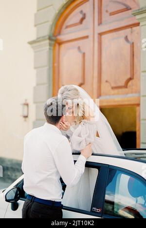 Le marié embrasse la mariée debout dans le toit ouvrant de la voiture Banque D'Images