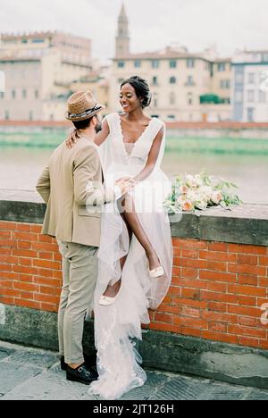 Le marié se trouve près de la mariée, assis sur une clôture en briques sur la rive de la rivière Banque D'Images