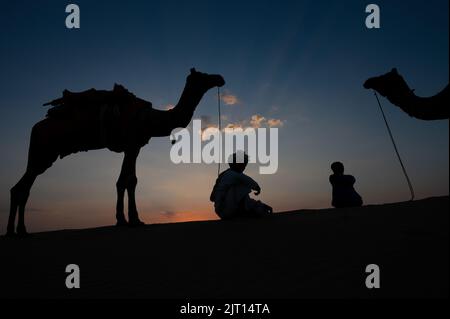 Silhouette de deux caméléers et de leurs chameaux sur les dunes de sable du désert de Thar, Rajasthan, Inde. Nuage avec coucher de soleil, ciel en arrière-plan. Banque D'Images