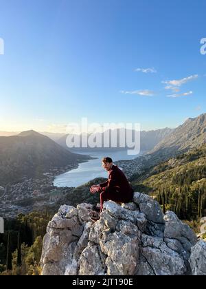 Budva, Monténégro - 01.08.22: L'homme en costume est assis sur un rocher sur la toile de fond de la baie de Kotor. Monténégro Banque D'Images