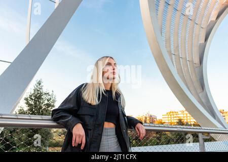 Belle fille blonde penchée dans un parc dans l'après-midi. Il y a un ciel bleu derrière elle Banque D'Images