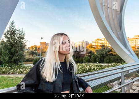 Belle fille blonde penchée dans un parc dans l'après-midi. Il y a un ciel bleu derrière elle Banque D'Images