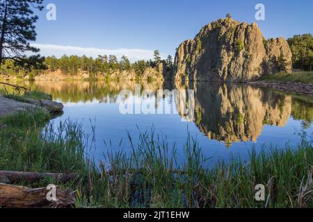 Des formations de granit reflétant la lumière du soleil couchant se reflètent elles-mêmes dans les eaux calmes du lac Legion, dans les Black Hills du Sud D. Banque D'Images