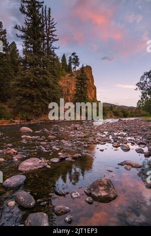 Un coucher de soleil de nuages roses se reflète sur l'eau douce et les pierres de la fourche sud du Rio Grande dans les montagnes San Juan du Colorado Banque D'Images