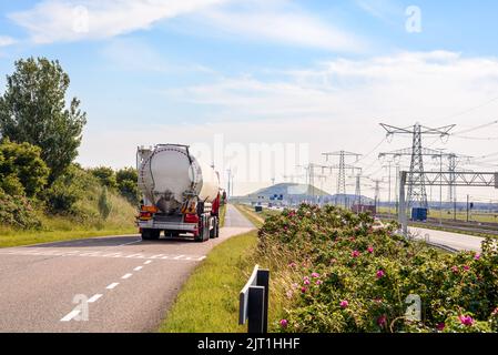 Camion-citerne sur une route étroite parallèle à une autoroute et à un chemin de fer dans une zone portuaire par une belle journée d'été. Les pylônes d'électricité sont en arrière-plan. Banque D'Images