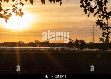 Coucher de soleil doré sur les silhouettes de serre avec pont et tour d'électricité pour l'énergie solaire dans les affaires agricoles sur campagne idyllique et rural Banque D'Images