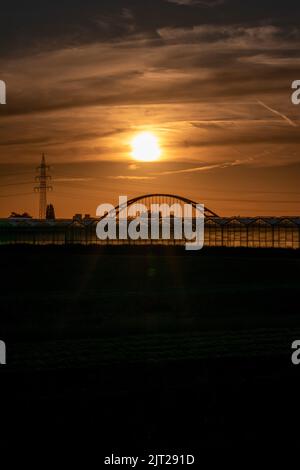 Coucher de soleil doré sur les silhouettes de serre avec pont et tour d'électricité pour l'énergie solaire dans les affaires agricoles sur campagne idyllique et rural Banque D'Images