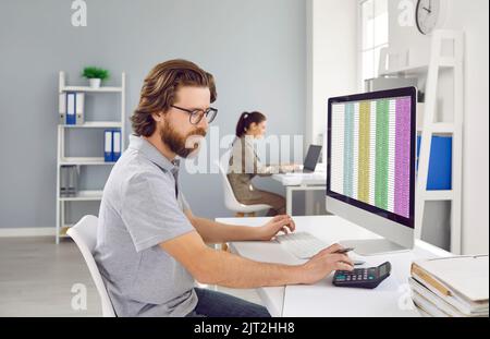 Le comptable masculin utilise la calculatrice pour calculer le rapport financier travaillant au bureau avec un ordinateur. Banque D'Images