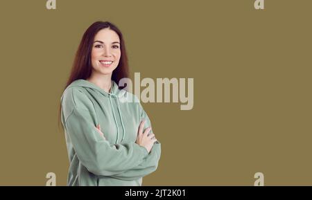 Bonne jeune femme dans des vêtements décontractés debout avec ses bras croisés sur fond d'espace de copie Banque D'Images