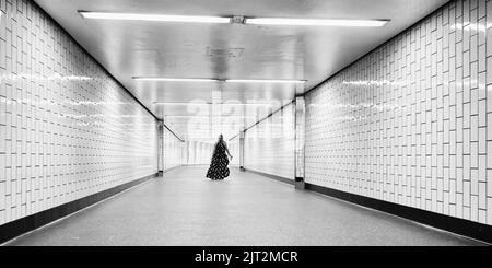 une femme vêtue d'été traverse un passage de métro solitaire Banque D'Images