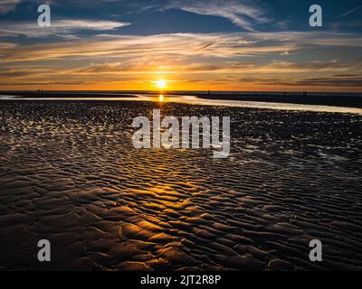 Ondule dans le sable à marée basse pendant un coucher de soleil spectaculaire Banque D'Images