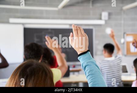 Vue arrière d'un élève en classe en levant la main pour poser une question pendant le cours. Une étudiante du secondaire pose une question à l'enseignant Banque D'Images