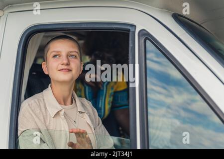 Jeune caucasien belle fille avec la tête rasée regardant hors de la fenêtre ouverte d'une camionnette de camping en admiration. Sa jeune femme africaine souriante avec des cheveux kinky sur le siège arrière. Photo de haute qualité Banque D'Images