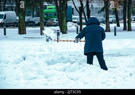 Homme avec une pelle élimine la neige à l'extérieur. Employé pendant le déneigement en ville d'hiver, nettoyage de la rue. Banque D'Images