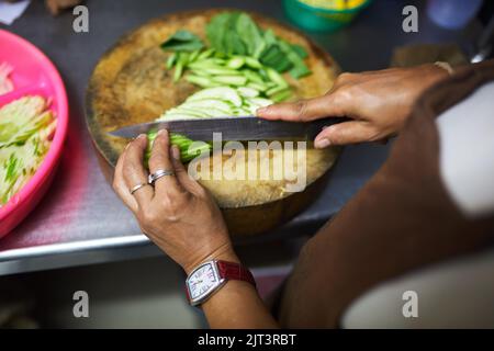 Trancher et trancher. Un chef inidentifiable se fait les mains comme elle coupe des légumes dans la cuisine. Banque D'Images