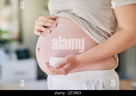 Réduire l'apparence des marques d'étirement naturellement. Une femme appliquant de la crème à son ventre enceinte. Banque D'Images
