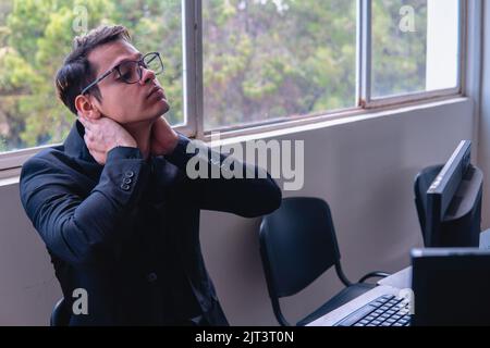 Employé de bureau fatigué après une journée de travail. Un homme à un bureau se crantant le cou. Employé de bureau travaillant sur l'ordinateur à son bureau. Photo de haute qualité Banque D'Images