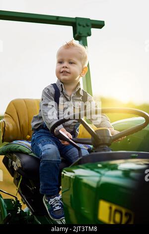 L'agriculture est dans son sang. Un adorable petit garçon qui monte sur un tracteur dans une ferme. Banque D'Images