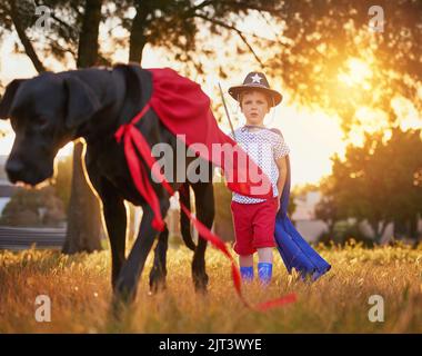 Méfiez-vous du chien et de son propriétaire. Un petit garçon et son chien portent des capes en jouant dehors. Banque D'Images