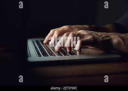 Rester anonyme derrière son clavier. Prise de vue en grand angle d'un homme non identifiable utilisant un ordinateur portable tard dans la nuit. Banque D'Images