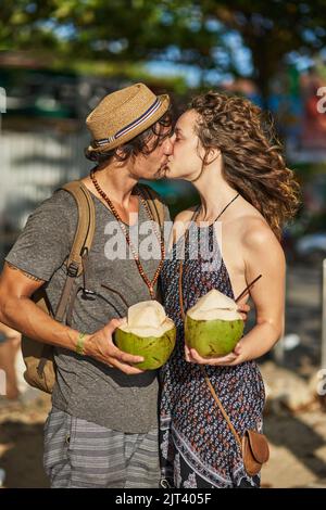 Vos baisers ont le goût de la noix de coco. Un jeune couple affectueux qui apprécie les cocktails tout en se relaxant sur la plage. Banque D'Images