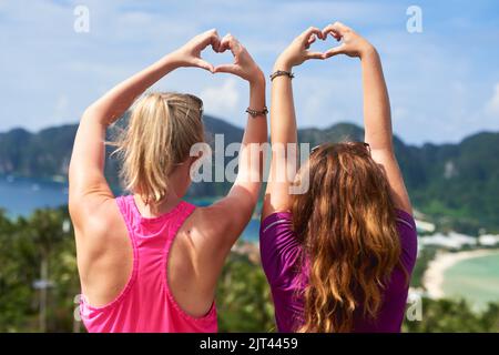 Continuez à aimer la vie. Vue arrière de deux jeunes femmes faisant un geste de coeur en faisant face à un paysage pittoresque. Banque D'Images