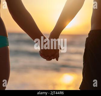 Un autre coucher de soleil romantique apprécié à la plage. Gros plan d'un jeune couple tenant les mains tout en regardant le coucher du soleil sur la plage. Banque D'Images