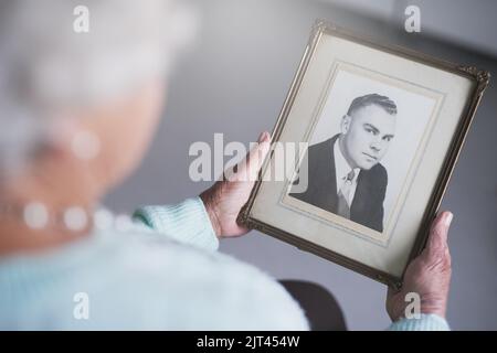 Il me manque un peu... une femme âgée qui regarde une vieille photo noir et blanc d'un homme. Banque D'Images