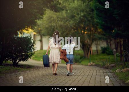 Personne ne le sait. Une petite fille et son frère s'éloignent en portant des valises et des jouets. Banque D'Images