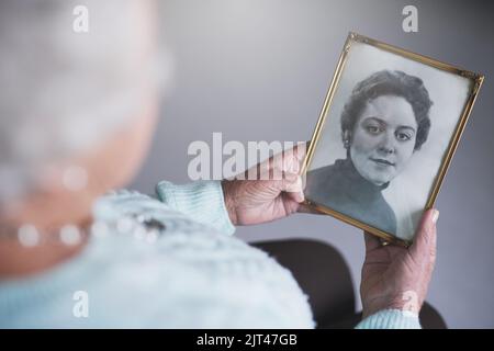 Se remémorant les années passées. Une femme âgée regardant une vieille photo noir et blanc d'une femme. Banque D'Images