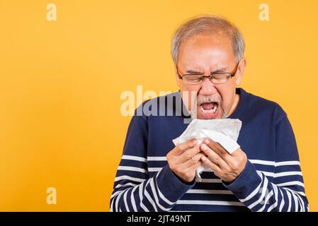 Portrait ancien homme soufflant nez avec studio de tissus tir isolé sur fond jaune, asiatique homme aîné froid ayant la grippe et éternuant de la maladie Banque D'Images