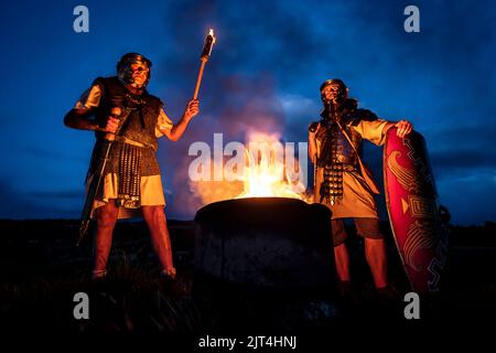 Martin Stiles (à gauche), membre du groupe d'histoire vivante romaine Secunda Augusta et Douglas Eckhart (à droite) de la Garde Antonine, se tiennent à côté d'un incendie lors de la reconstitution d'une attaque de nuit au fort romain de Chesters, au mur d'Hadrien, à Hexham. Date de la photo: Samedi 27 août 2022. Banque D'Images