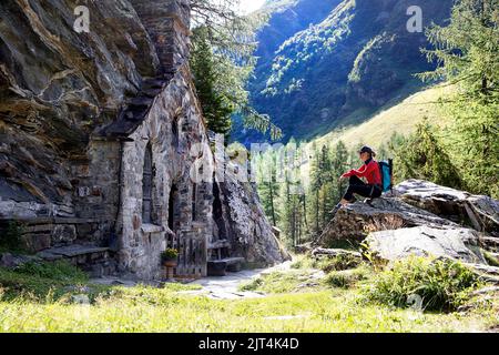 Femme randonneur assise en face de la chapelle rocheuse Maria Schnee près d'Innergschlöß dans la vallée de Gschlosstal, Parc national Hohe Tauern, Tyrol oriental, Autriche Banque D'Images