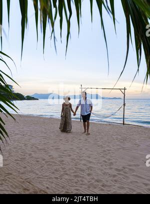 Hommes et femmes marchant sur la plage de Pattaya au coucher du soleil sur la plage de Ban Amphur en Thaïlande. Couple marchant sur une plage tropicale avec palmiers et hamac au coucher du soleil Banque D'Images