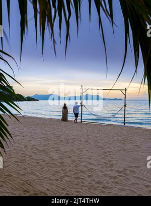 Hommes et femmes marchant sur la plage de Pattaya au coucher du soleil sur la plage de Ban Amphur en Thaïlande. Couple marchant sur une plage tropicale avec palmiers et hamac au coucher du soleil Banque D'Images