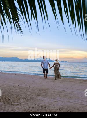 Hommes et femmes marchant sur la plage de Pattaya au coucher du soleil sur la plage de Ban Amphur en Thaïlande. Couple marchant sur une plage tropicale avec palmiers et hamac au coucher du soleil Banque D'Images