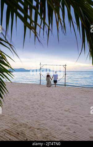 Hommes et femmes marchant sur la plage de Pattaya au coucher du soleil sur la plage de Ban Amphur en Thaïlande. Couple marchant sur une plage tropicale avec palmiers et hamac au coucher du soleil Banque D'Images