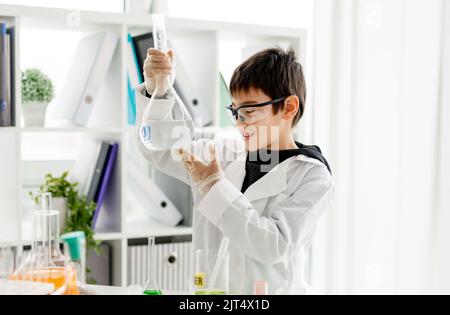 Garçon d'école portant des lunettes de protection faisant une expérience de chimie regardant le tube dans la classe de sciences élémentaires. Pupille intelligente analysant les lici transparents Banque D'Images