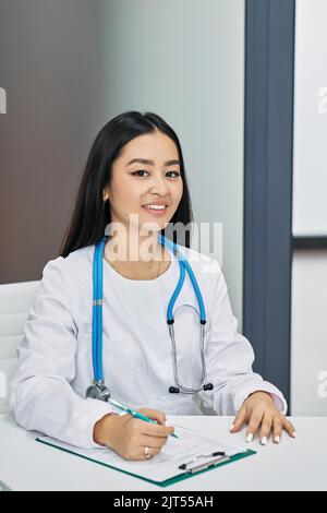 Portrait d'une femme généraliste asiatique vêtue d'un manteau blanc assise sur son lieu de travail à la clinique médicale. la consultation médicale Banque D'Images
