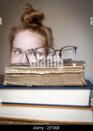 Une grande pile de livres avec des verres sur le dessus. De derrière les piles à travers les lunettes ressemble une jeune fille européenne drôle à cheveux rouges vert-yeux verts Banque D'Images
