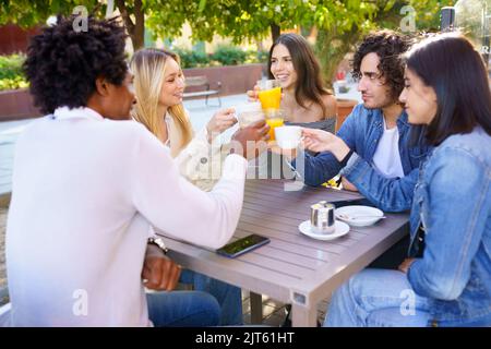 Groupe multiethnique d'amis qui toaster avec leurs boissons tout en prenant un verre ensemble. Banque D'Images