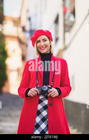 Content femme élégante avec un appareil photo au cou souriant dans la rue de la ville Banque D'Images