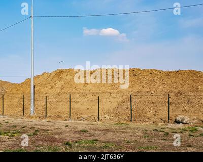 Travaux de terrassement en extérieur avec une grande pile de sable derrière la clôture et un paysage céleste. Banque D'Images